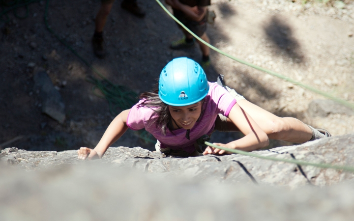 an outward bound student focuses while climbing a rock wall